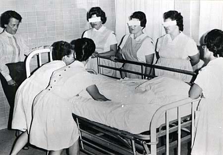 Nurses standing over a patient in a hospital bed, their eyes blacked out in the original print